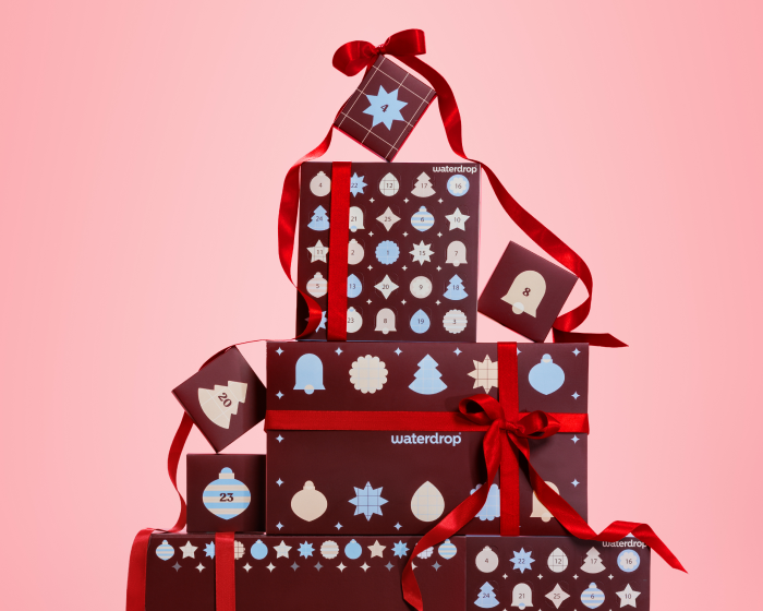 Stack of gift boxes with patterned wrapping and red ribbons on a pink background.