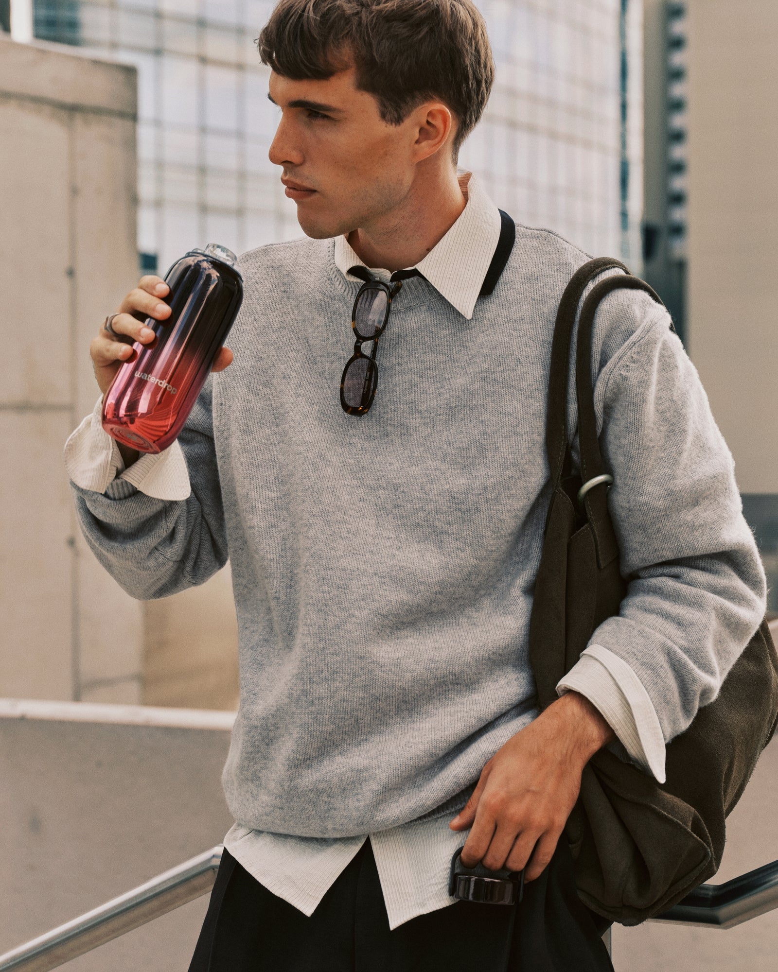 Man in a gray sweatshirt over a white shirt carries a backpack while drinking from a gradient tumbler.